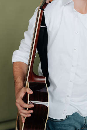 a man in a white T-shirt holds an acoustic guitar in his hands. Musician