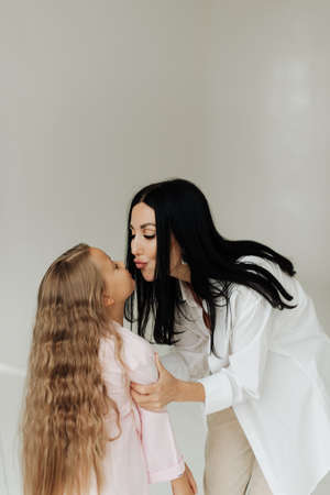 beautiful young brunette mom kissing her daughter with long blond hair on a white backgroundの写真素材