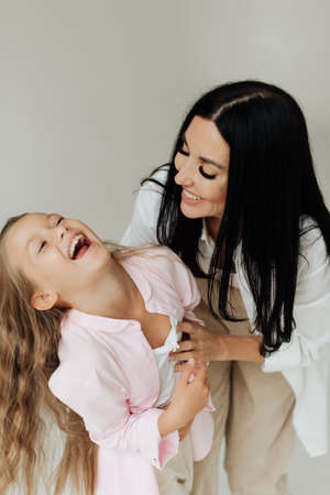 beautiful brunette mom and daughter laugh on the background of a white wallの写真素材