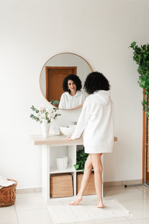 Woman with curly black hair with bare legs looks in a round mirrorの写真素材