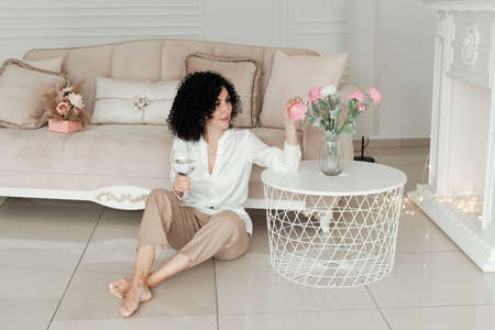 A woman with african curls sits on the floor next to a coffee table on which there are flowers