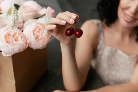 A girl holding ripe cherries in her hands on the background of a bouquet of pink flowersの写真素材