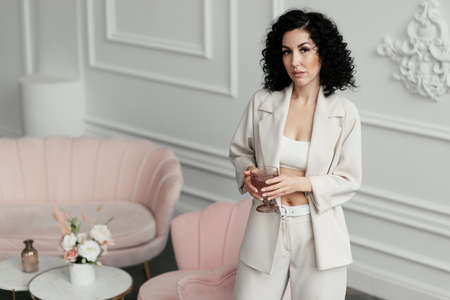 Attractive woman in a suit with a naked belly holds a pink glass in her handsの写真素材
