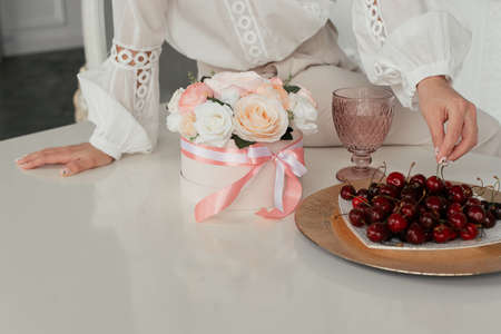 a bouquet of pastel flowers stands on a white table next to a plate of cherriesの写真素材
