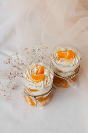 2 ice creams in a transparent cup decorated with tangerines on a white tableの写真素材
