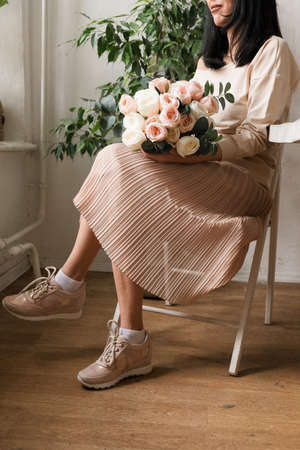 beautiful young brunette girl with a bouquet of flowers sits on a chairの写真素材
