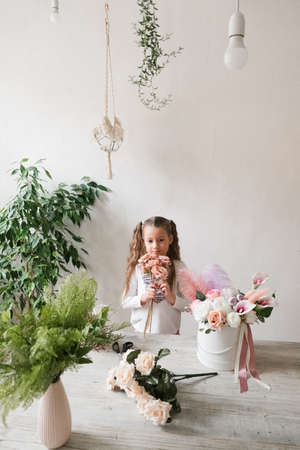 cute little girl in a white t-shirt with braids collects a bouquet of flowers at the tableの写真素材