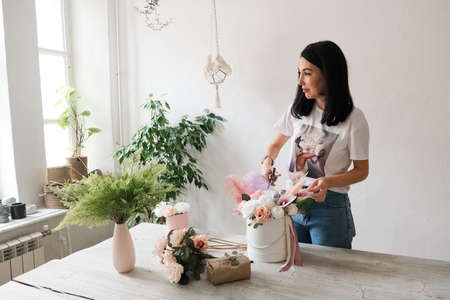 beautiful young brunette girl makes a bouquet of flowers with her own hands on the table florist at workの写真素材