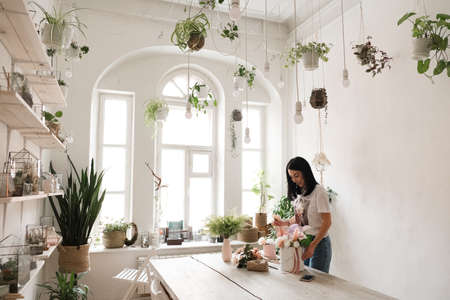 florist work beautiful brunette girl and a bouquet of flowers on the table in a stylish roomの写真素材