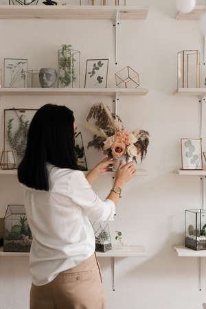 stylish brunette in white shirt decorates the room with flowers vase on the shelfの写真素材