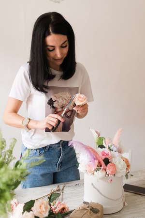 the florist collects a bouquet of flowers beautiful smiling brunette girl in a white t-shirt with flowersの写真素材