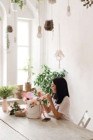 beautiful young girl brunette florist works at the table collects a bouquet of flowersの写真素材