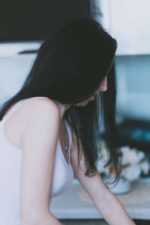 beautiful young brunette girl in a purple top in profile in the kitchenの写真素材