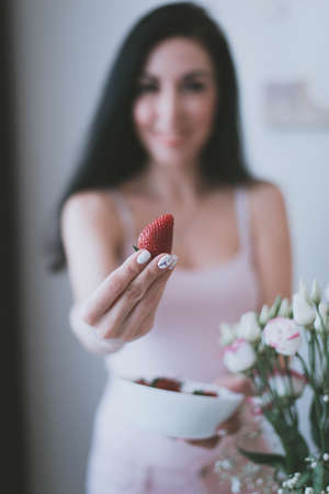 red strawberry in the hands of a young brunette girl in a purple topの写真素材