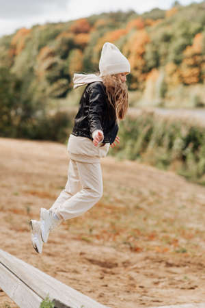 cute little girl in a white hat and black leather jacket fooling around in an autumn parkの写真素材