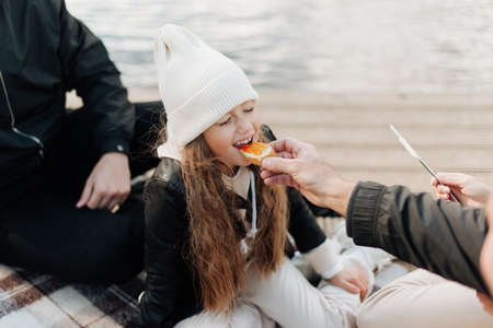 parents feed their little daughter in a white hat with a sandwich happy familyの写真素材