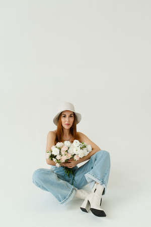 beautiful girl with a bouquet of flowers in a panama hat and blue jeans on a beige solid backgroundの写真素材