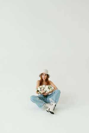beautiful girl with a bouquet of flowers in a panama hat and blue jeans on a beige solid backgroundの写真素材