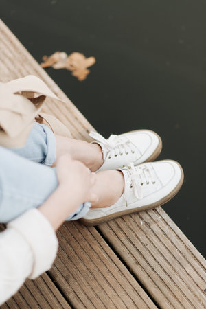 stylish female legs in white sneakers on a background of a wooden surface and waterの写真素材