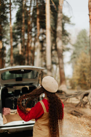 stylish girl with long hair and a white beret stands in the autumn forest against the backdrop of a large carの写真素材