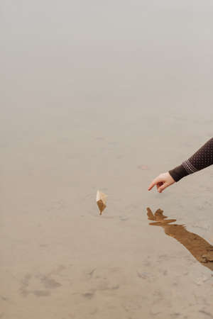 a small paper boat floats on the water close-up and a man's handの写真素材