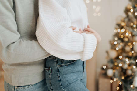 stylish man and girl in sweaters and blue jeans hugging on the background of the Christmas treeの写真素材