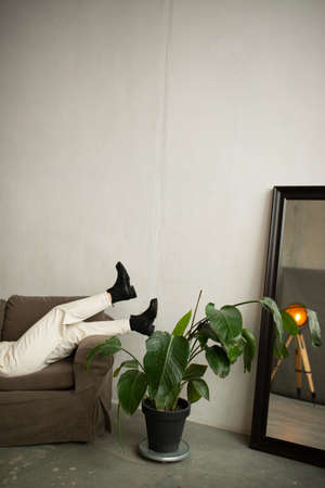 stylish girl in white pants and big black shoes lies on the sofa near a flower and a mirrorの写真素材