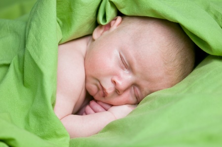 newborn boy sleeping under green sheetの写真素材