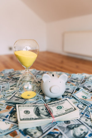 Piggy moneybox with dollar cash and sand clock closeup. Financial concept