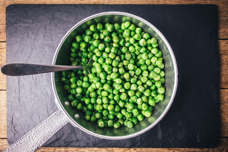 Green peas on silver frying pan on black slate plate. Food photographyの写真素材