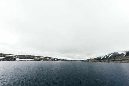 Typical norwegian landscape with snowy mountains and clear lake near the famous Trolltunga rock,...