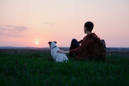 Teenager on green lawn with small white dog. Friendship and travel conceptの写真素材