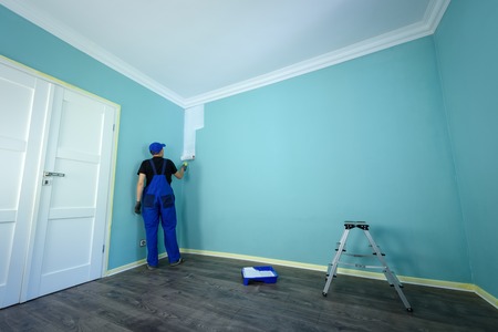 Man in a working overall is painting the wall in white colorの写真素材