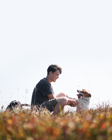 Teenager on autumn lawn with small white dog. Friendship and travel concept