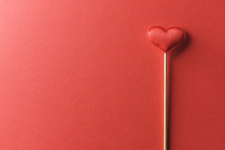 Red textile heart on wooden stick closeup. Valentines day background, creative texture and love conceptの写真素材