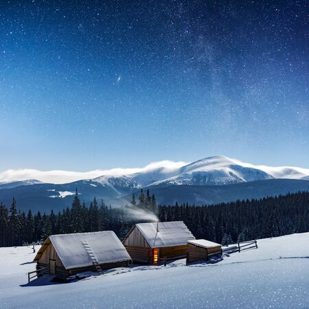Fantastic night landscape glowing by milky way. Dramatic wintry scene with snowy house. Carpathian...