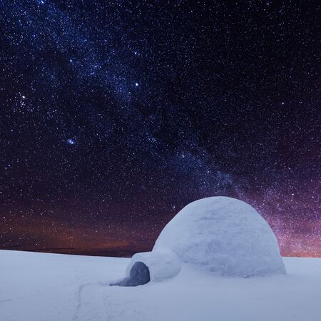 Wintry scene with snowy igloo and milky way in night sky. Fantastic winter landscape glowing by star light. Santa house from snow, ideal New Year and Christmas backgroundの写真素材