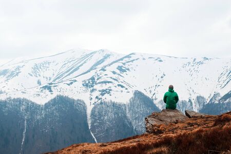 Man in green jacket sitting on rock in spring mountains. Travel concept. Landscape photography