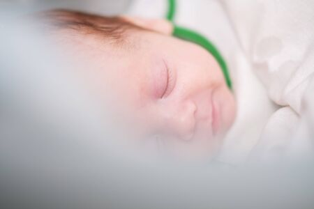 Sleeping and smiling newborn baby boy under white carpet closeup.