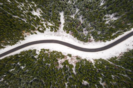 Flight over the winter mountains with road serpentine and snowy forest.の写真素材