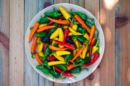 Mixed colours hot peppers on wooden plate closeup. Food photography