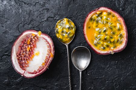 Slised passion fruit with silver spoons on black concrete background. Food photographyの写真素材