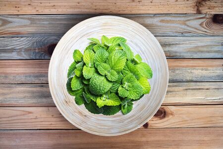 Round bamboo plate with mint bunch on a wooden table closeup. Food photography background