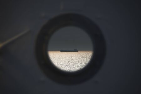 Lonely fishing ship trawler boat on ocean water. View from the round window from the cabin. Calm clear sea sunny weather. Beautiful horizon of seascapeの写真素材
