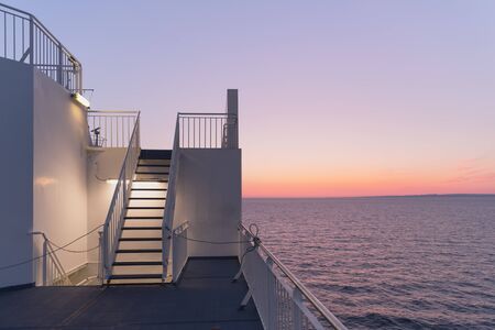 Deck of a cruise ship during sunset. Calm ocean and clear pink sky in evening time. Cruise vacations background. Minimalism in photographyの写真素材