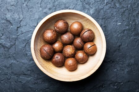 Dried organic Macadamia nuts in wooden bowl closeup. Studio macro shoot. Black concrete backgroundの写真素材
