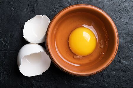 Chicken yolk from broken organic egg in brown plate on black concrete background. Food photography