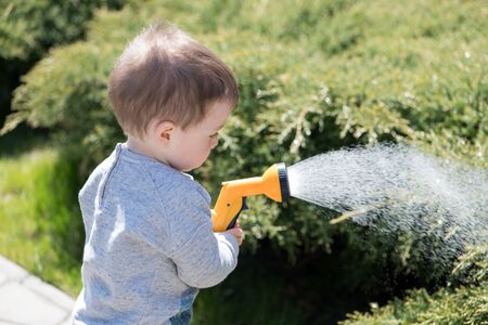 Small boy with watering can watering trees on backyard. Happy childhood conceptの写真素材