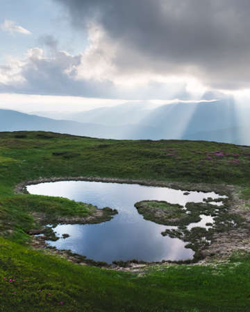 Mountain lake on sunrise time. Picturesque summer landscape with green mountain hills and sun rays...