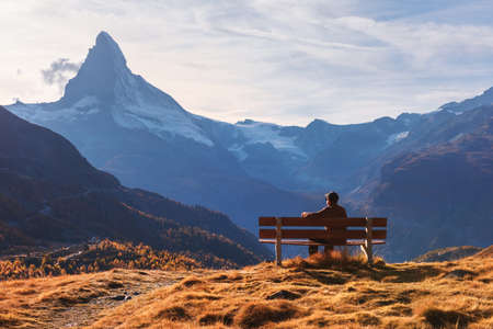 Picturesque view of Matterhorn peak and tourist sitting on wooden bench in Swiss Alps. Zermatt resort location, Switzerland. Landscape photographyの写真素材